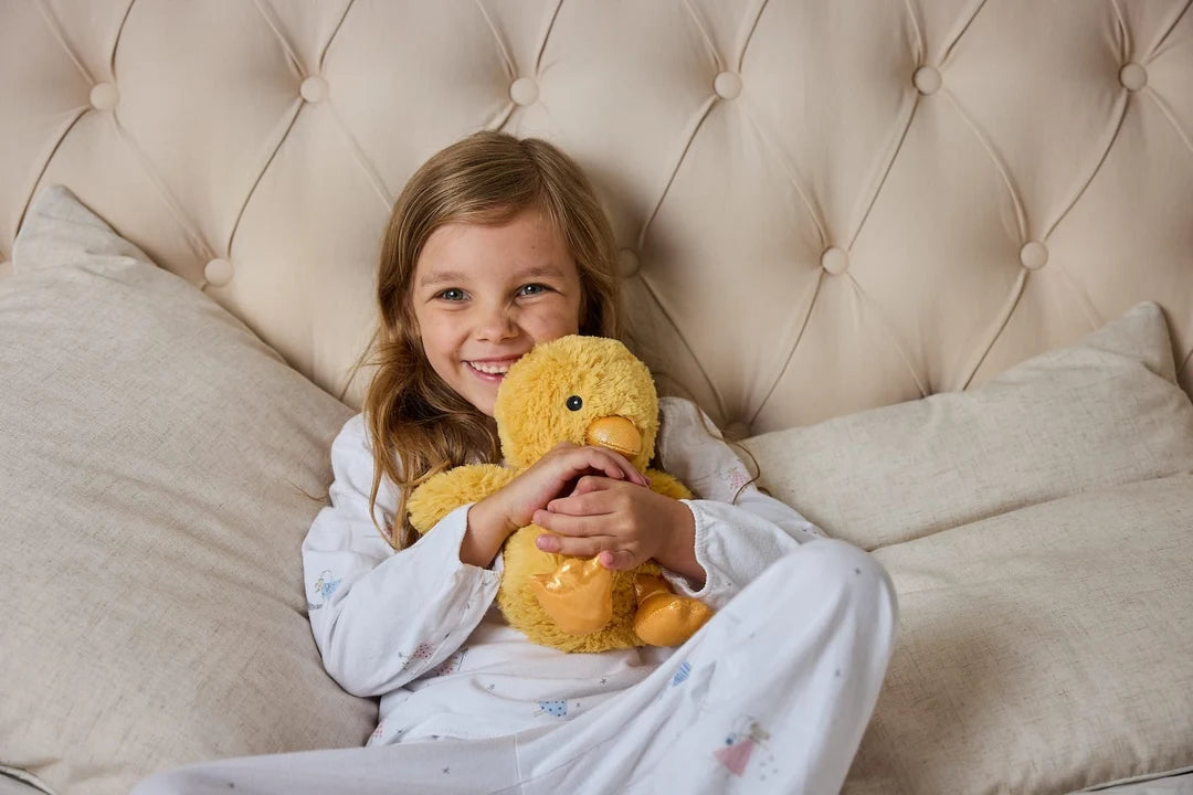 Child in bed holding a Warmies Junior chick heatable lavender plush toy