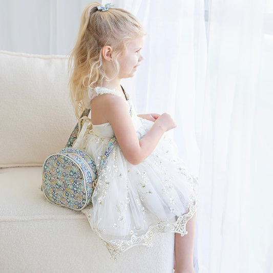 Girl sitting on a sofa wearing the Suzanne crossbody bag