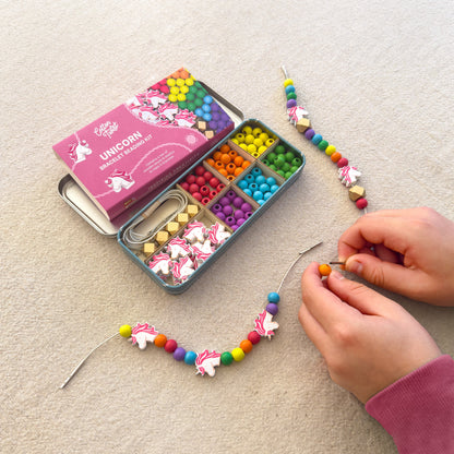 Hands threading unicorn and rainbow wooden beads from the Unicorn Beading Kit tin